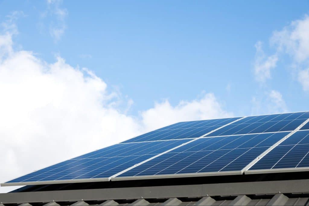 Zonnepanelen op een dak onder een blauwe lucht die stroom opwekken voor de laadpaal.