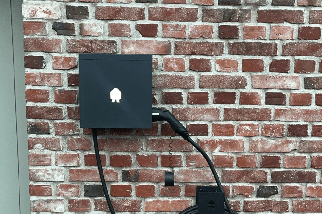 Smappee EV Wall thuislaadpaal in het zwart met ingeplugde laadkabel tegen een bakstenen muur.