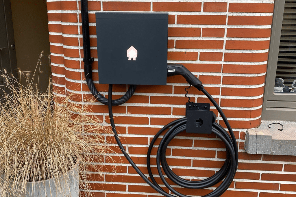 Zwarte Smappee EV Wall laadpaal met opgerolde laadkabel gemonteerd tegen een bakstenen gevel.